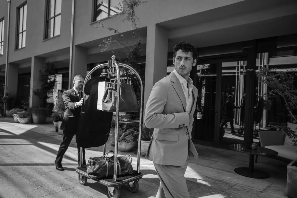 Black and white arrival scene: a guest and a porter with a luggage trolley outside the hotel