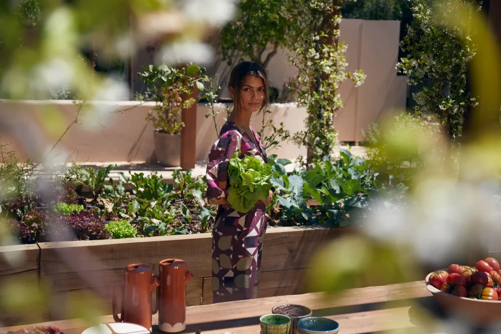 A woman gathering lettuce in the hotel kitchen garden, seen through foliage