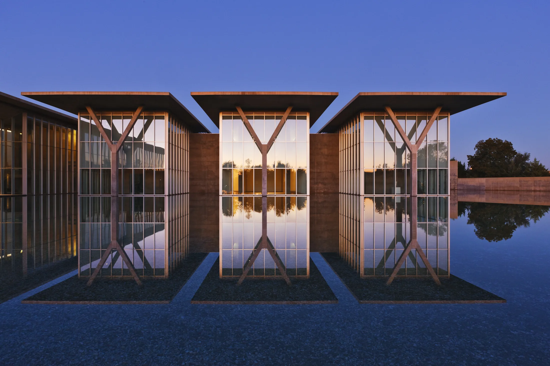 Modern pavilion with Y-shaped columns reflected in a still pool at dusk