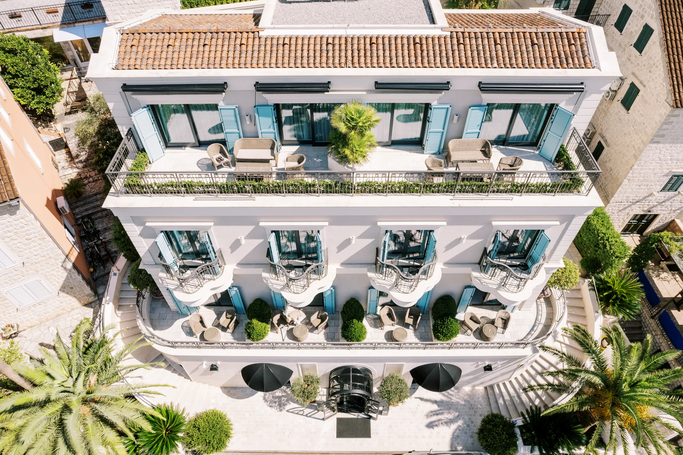 Aerial view of a classic hotel facade with planted terraces and palm trees