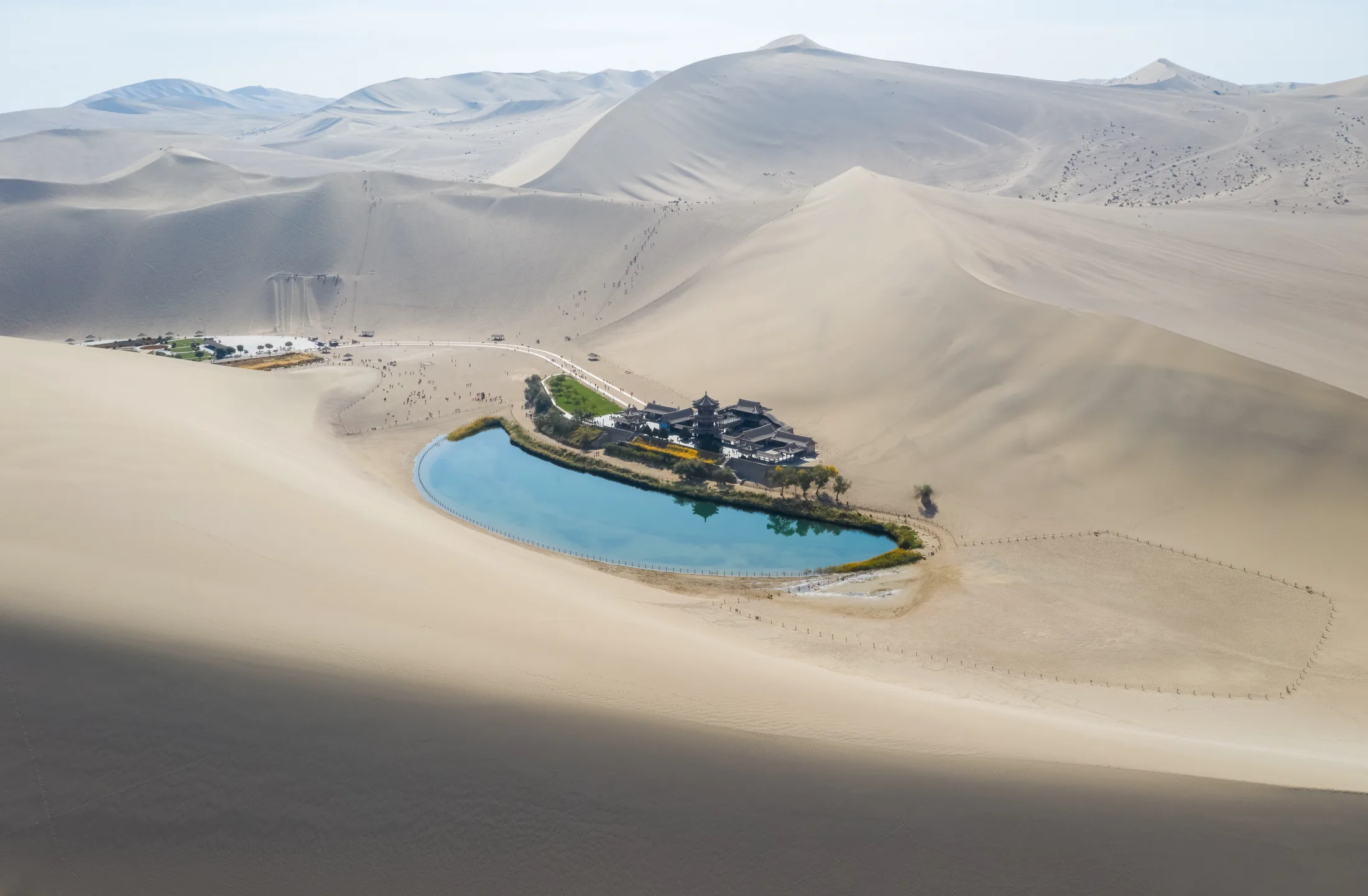 PSC-News-Next-Traveller-06 · Permanent State of Creation Desert oasis lake with a traditional building among sand dunes