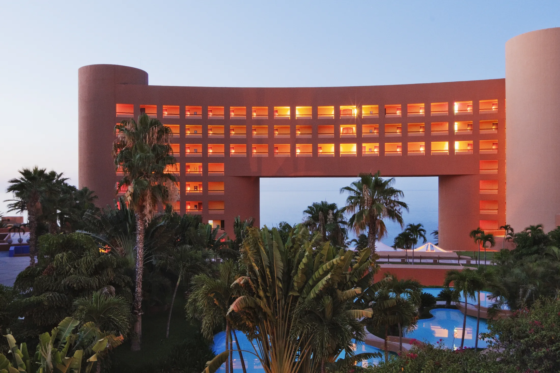 PSC-News-Next-Traveller-08 · Permanent State of Creation Luxury hotel with a glowing arched facade rising above palm trees